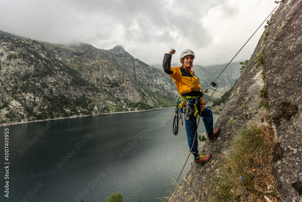 Obraz premium A man in a yellow jacket is standing on a rock near a body of water. He is wearing a helmet and he is enjoying the view