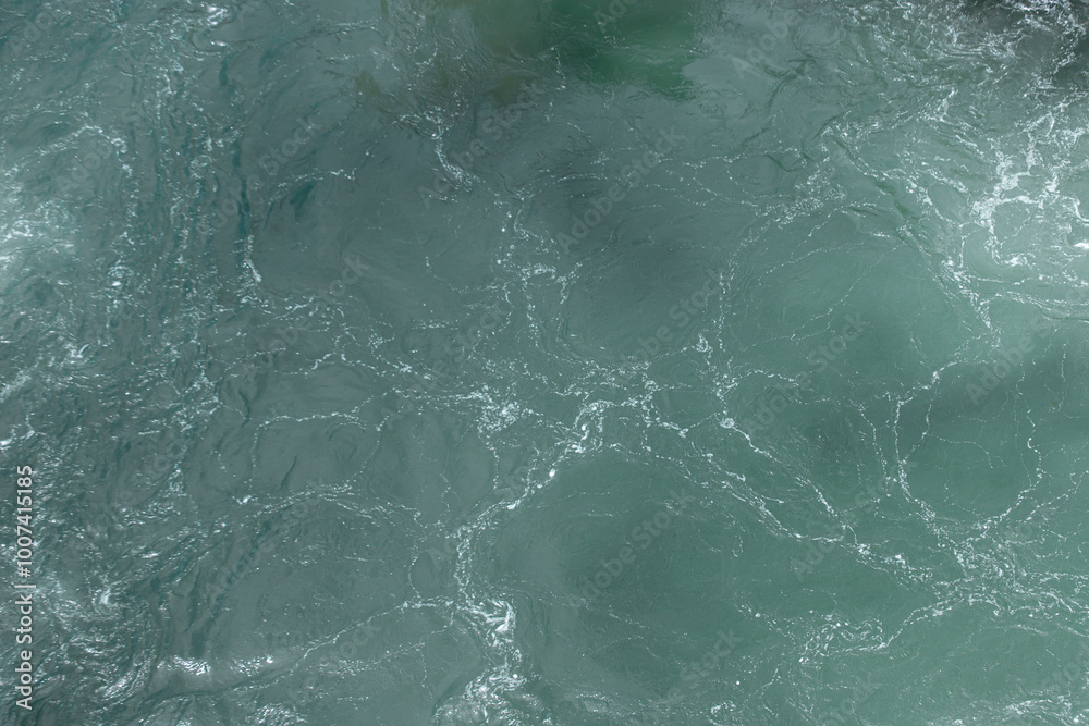 Obraz premium Detailed close-up of a turbulent green ocean water surface, showing swirling patterns, textures, and white foam on the waves.