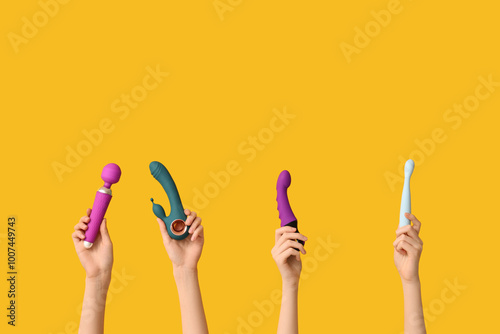 Female hands with different vibrators on yellow background