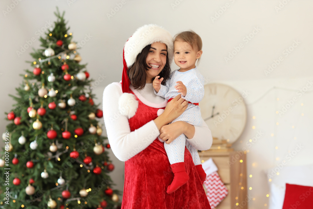 Happy mother in Santa costume holding her little baby at home on Christmas eve