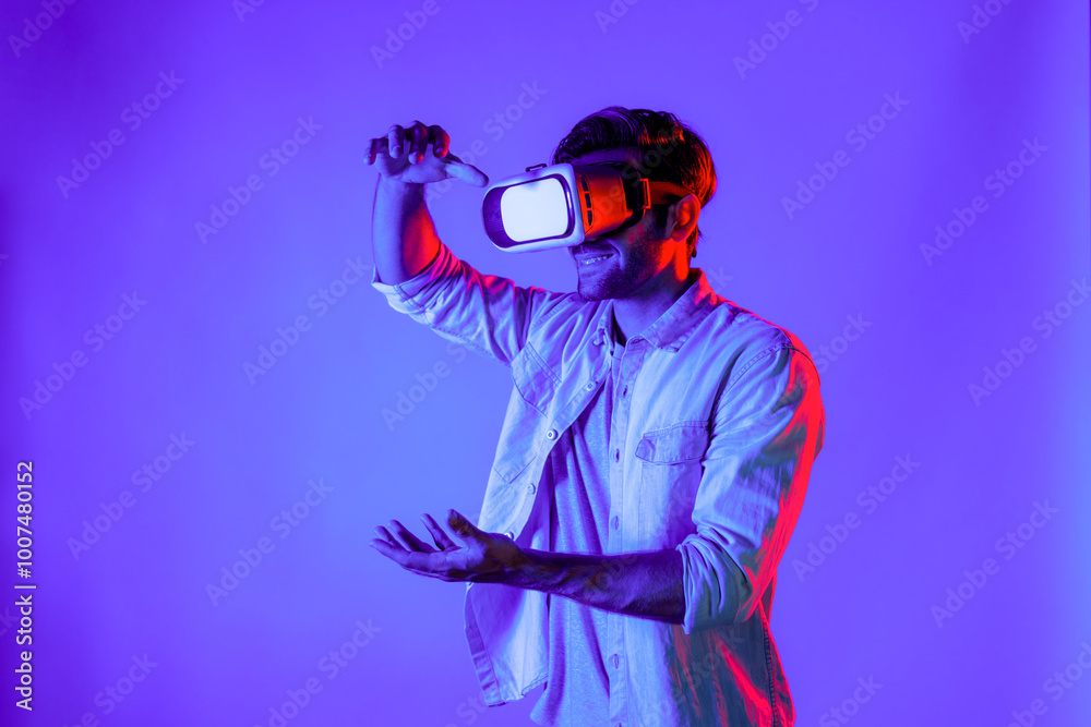Side view of happy man holding and moving gesture while using VR goggle. Happy person using headset and goggle while enter virtual world or metaverse with neon light background. Technology. Deviation. Side view of happy man holding and moving gesture while using VR goggle. Happy person using headset and goggle while enter virtual world or metaverse with neon light background. Technology. Deviation.