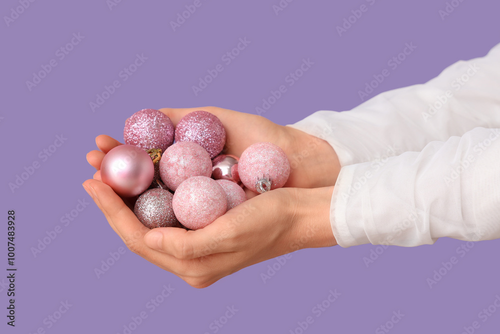 Female hands full of beautiful Christmas balls on lilac background, closeup Female hands full of beautiful Christmas balls on lilac background, closeup