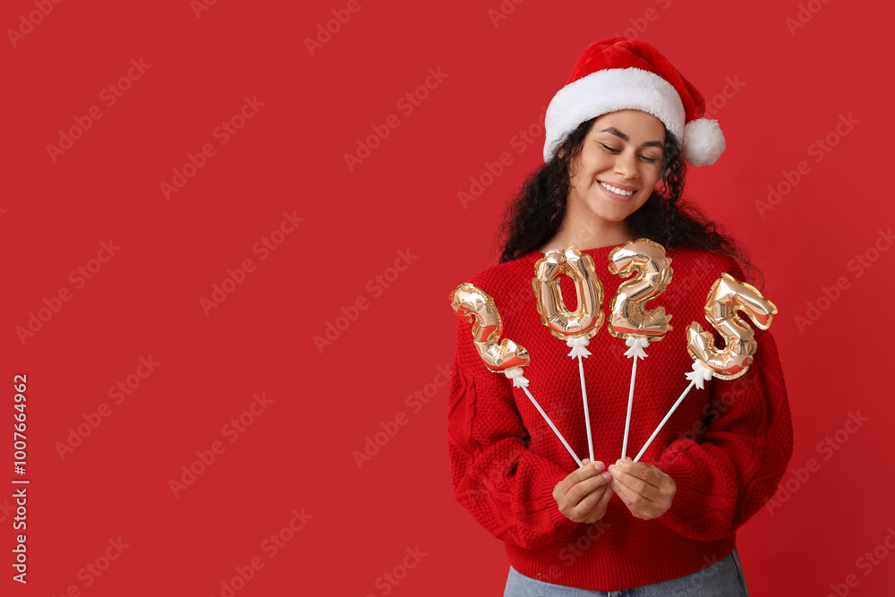 Happy African-American woman in Santa hat and with figure 2025 made of balloons on red background. New Year celebration Happy African-American woman in Santa hat and with figure 2025 made of balloons on red background. New Year celebration