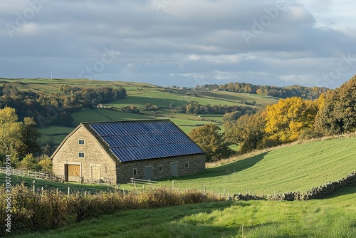 A stone barn with solar panels on the roof sits on a green hillside with autumnal foliage.