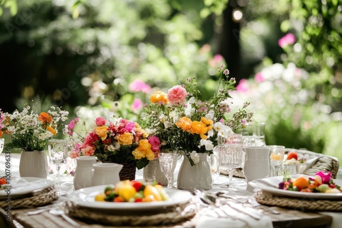 A table set for a summer meal in a garden, with flowers in vases and a plate of fruit.