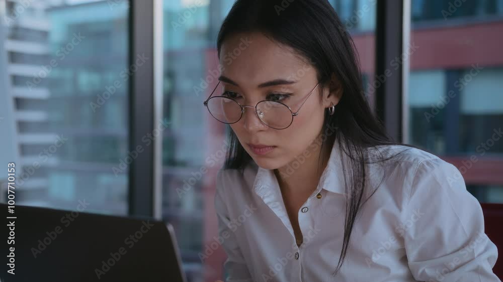 Asian businesswoman in glasses works on laptop in office Asian businesswoman in glasses works on laptop in office