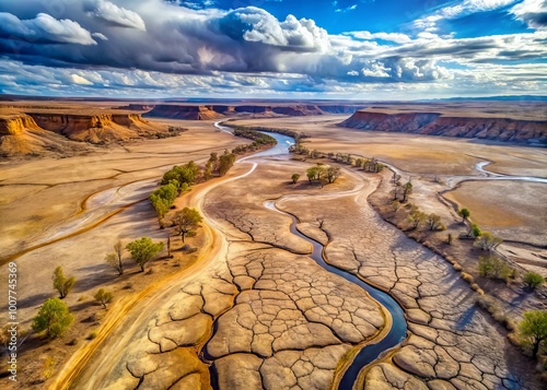 Aerial view of a dry, cracked riverbed winding through a vast, barren landscape, surrounded by rocky outcroppings and