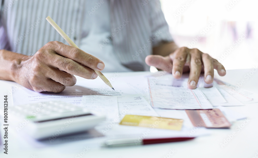 Asian man holding pencil calculate monthly expenses from receipt and many bill of various expenses after spending via credit card and must be pay back soon, Close-up shot Asian man holding pencil calculate monthly expenses from receipt and many bill of various expenses after spending via credit card and must be pay back soon, Close-up shot