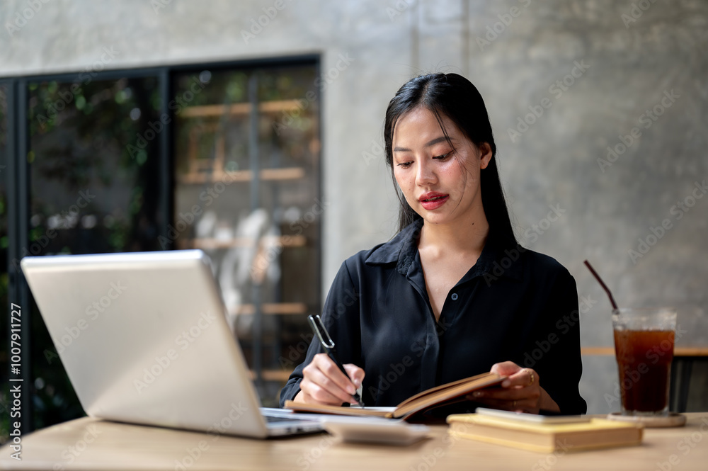 A beautiful Asian businesswoman focusing on her work as she takes notes in a book in a coffee shop. A beautiful Asian businesswoman focusing on her work as she takes notes in a book in a coffee shop.