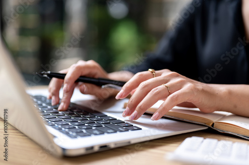 A close-up of a businesswoman's hand typing on a laptop keyboard while working at a table indoors.