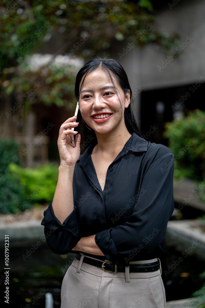 A charming Asian businesswoman is having a conversation on the phone while relaxing in a garden. A charming Asian businesswoman is having a conversation on the phone while relaxing in a garden.