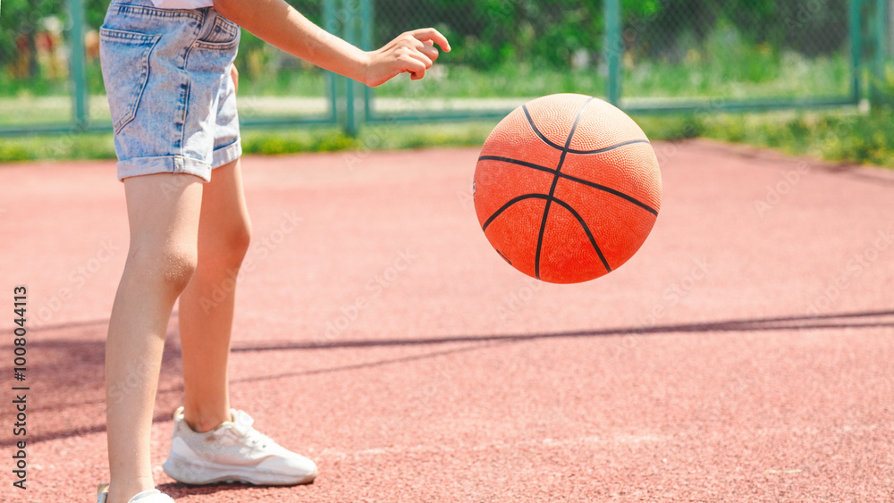 Child girl practicing exercise hitting basketball ball training on court in city.