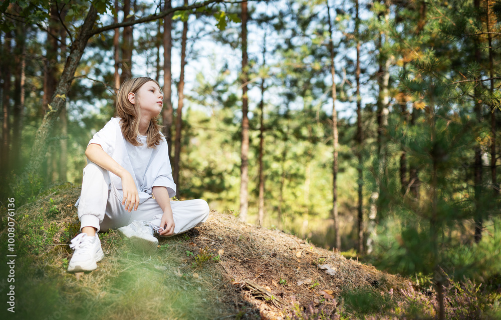 Young girl enjoying a sunny day in a forest clearing while sitting on a grassy mound surrounded by trees and nature Young girl enjoying a sunny day in a forest clearing while sitting on a grassy mound surrounded by trees and nature