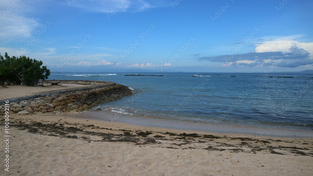 The horizons blue sea meets white sand and land dotted by trees against a bright sky. The horizons blue sea meets white sand and land dotted by trees against a bright sky.