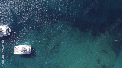 Aerial top down shot of two catamarans anchored in the shallow waters of a beach. Flying sideways to reveal swimmers in the crystal clear waters. photo