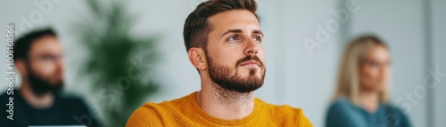 Focused man in yellow sweater listening attentively in classroom setting, surrounded by peers. atmosphere is engaging and thoughtful, highlighting moment of learning