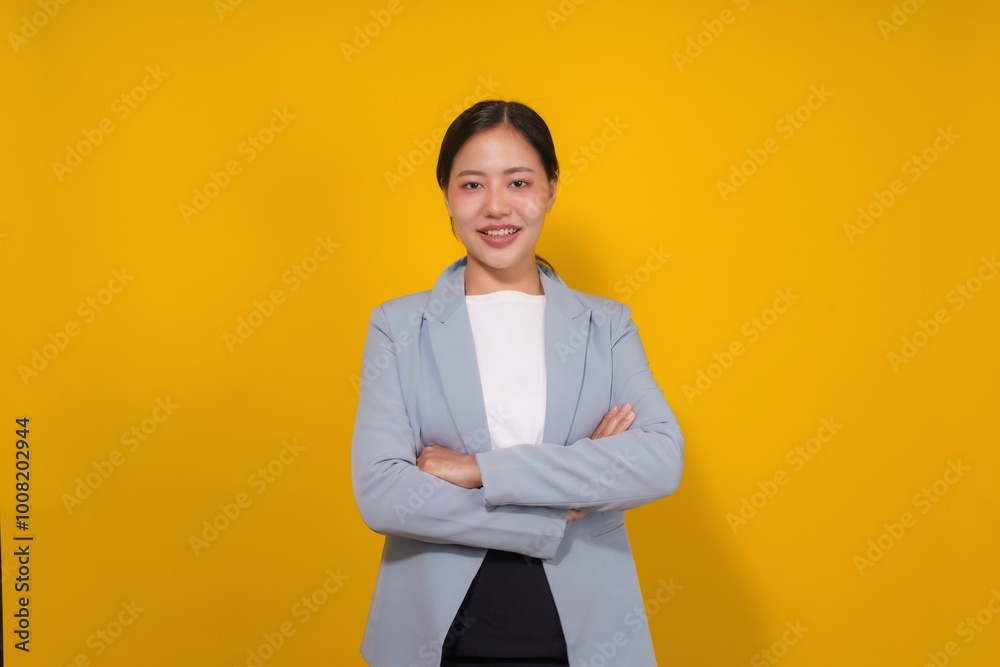 Young asian woman wearing a blue blazer over a white shirt is smiling with her arms folded on a yellow background Young asian woman wearing a blue blazer over a white shirt is smiling with her arms folded on a yellow background