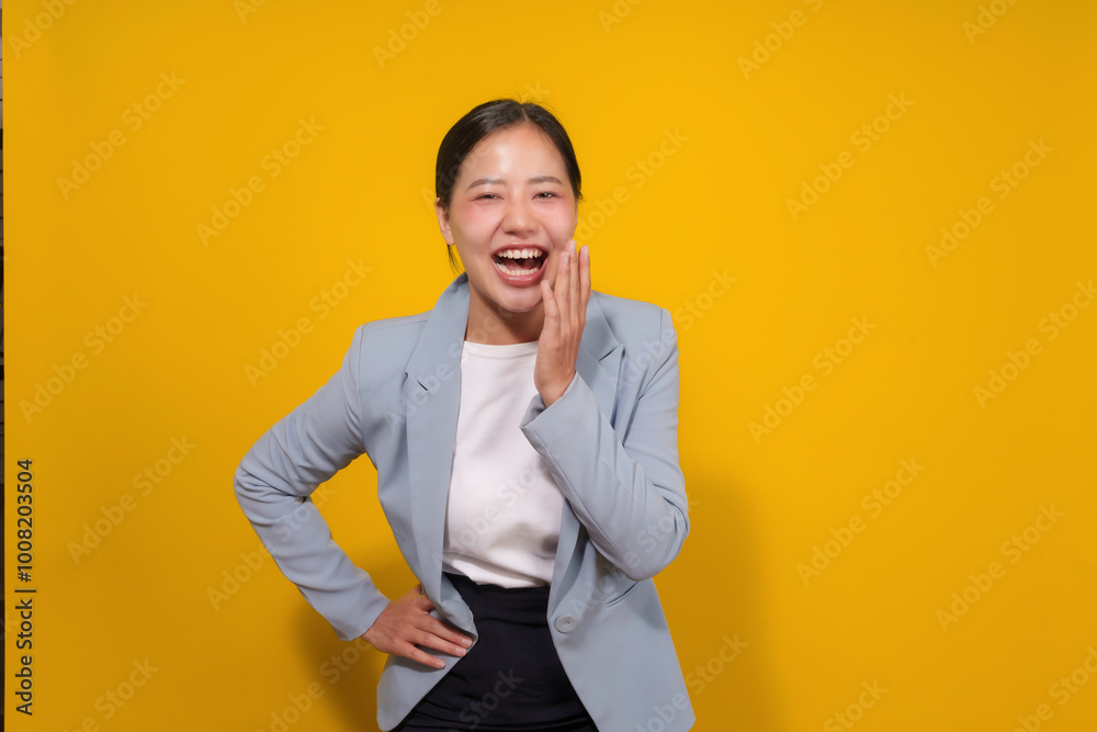 Young asian businesswoman in a blue blazer is laughing hysterically with her hand on her face over a yellow background Young asian businesswoman in a blue blazer is laughing hysterically with her hand on her face over a yellow background