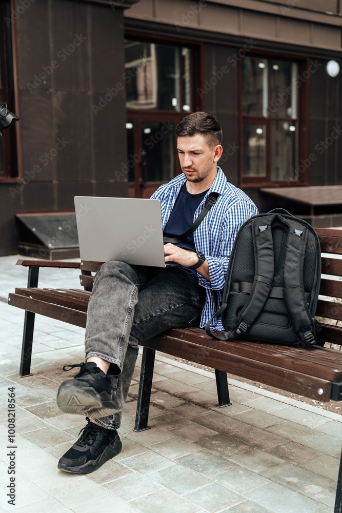 Young man working on a laptop while seated on a bench outside Young man working on a laptop while seated on a bench outside