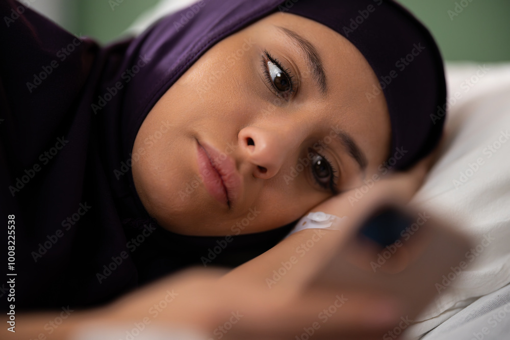 Young woman of Arab descent resting in a healthcare setting, holding a smartphone.
