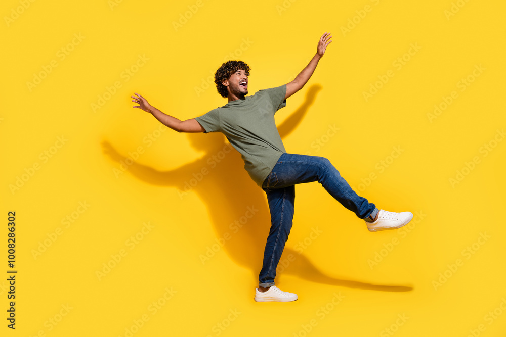 Full size photo of positive guy dressed khaki t-shirt jeans raising palms up dancing look empty space isolated on yellow color background Full size photo of positive guy dressed khaki t-shirt jeans raising palms up dancing look empty space isolated on yellow color background
