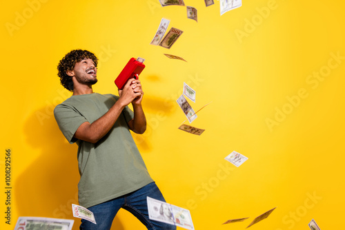 Photo of eccentric guy with wavy hair dressed khaki t-shirt throwing dollars with gun celebrate sale isolated on yellow color background photo