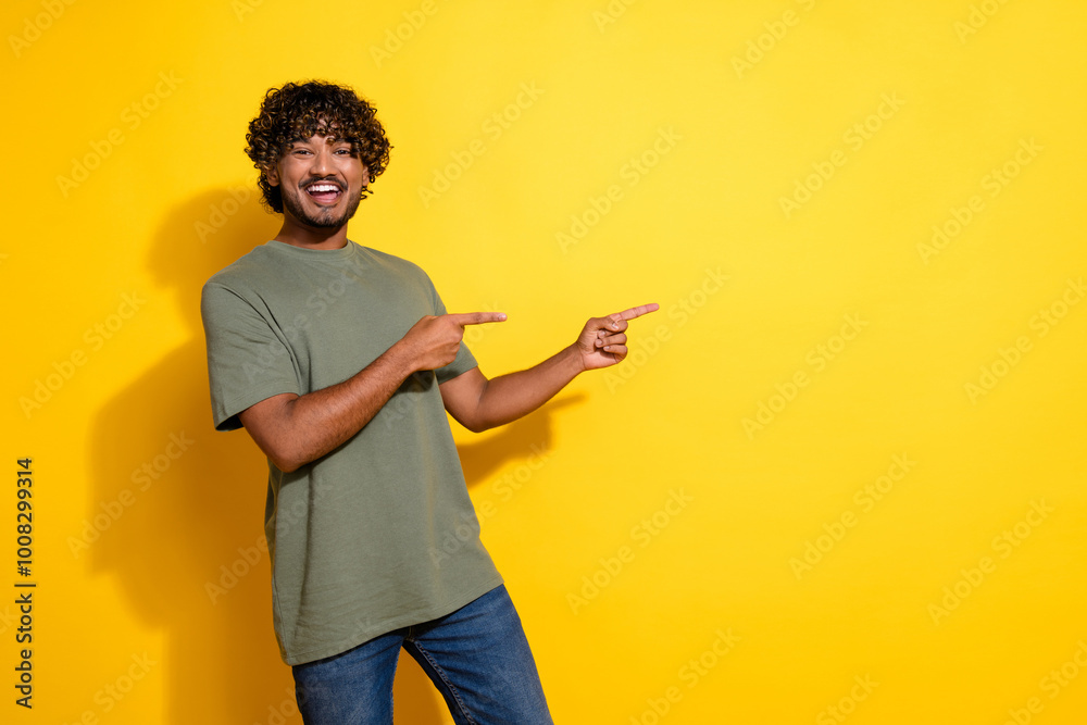 Photo of funky cheerful guy with curly hairstyle dressed khaki shirt indicating at offer empty space isolated on yellow color background Photo of funky cheerful guy with curly hairstyle dressed khaki shirt indicating at offer empty space isolated on yellow color background