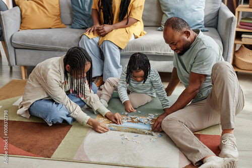 Family of four sitting on floor engaging in puzzle activity while showing close bond and teamwork in well-furnished and cozy living room setting