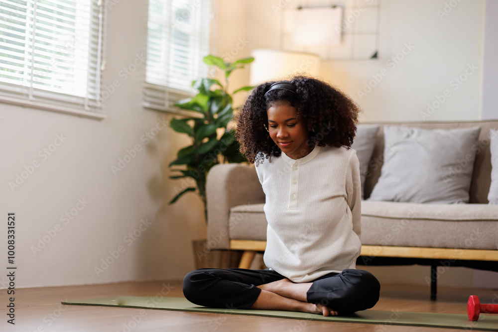 A curly African American woman in activewear practices yoga in a serene living room Meditating at Home with Headphones setting.
A curly African American woman in activewear practices yoga in a serene living room Meditating at Home with Headphones setting.