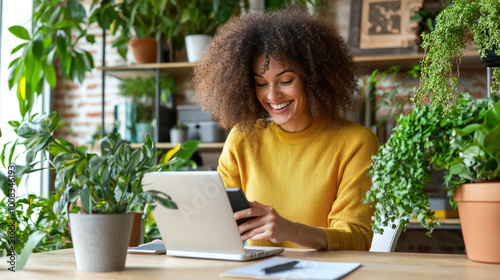 woman smiles as she checks her phone while sitting at desk surrounded by lush green plants. bright and cheerful atmosphere enhances her joyful expression