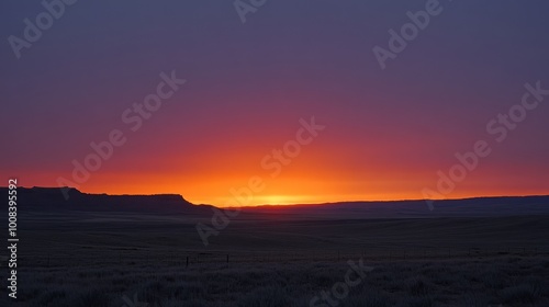 A vibrant sunrise over a vast, flat landscape, with a distant mountain range silhouetted against the fiery sky.