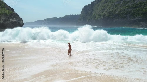 A slender woman on the shore of a stormy sea at Kelinking Beach in Nusa Penida. A woman on the shore of a popular beach in Indonesia photo