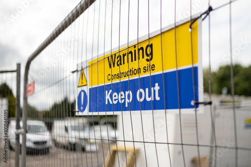 Blue and Yellow Warning Construction Site Keep Out sign on temporary heras fence panel and white steel storage container background