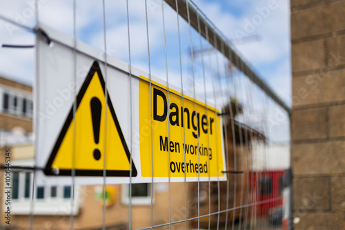 Yellow and black Danger Men Working Overhead triangle warning sign on construction site temporary heras fence panel and white steel storage container photo