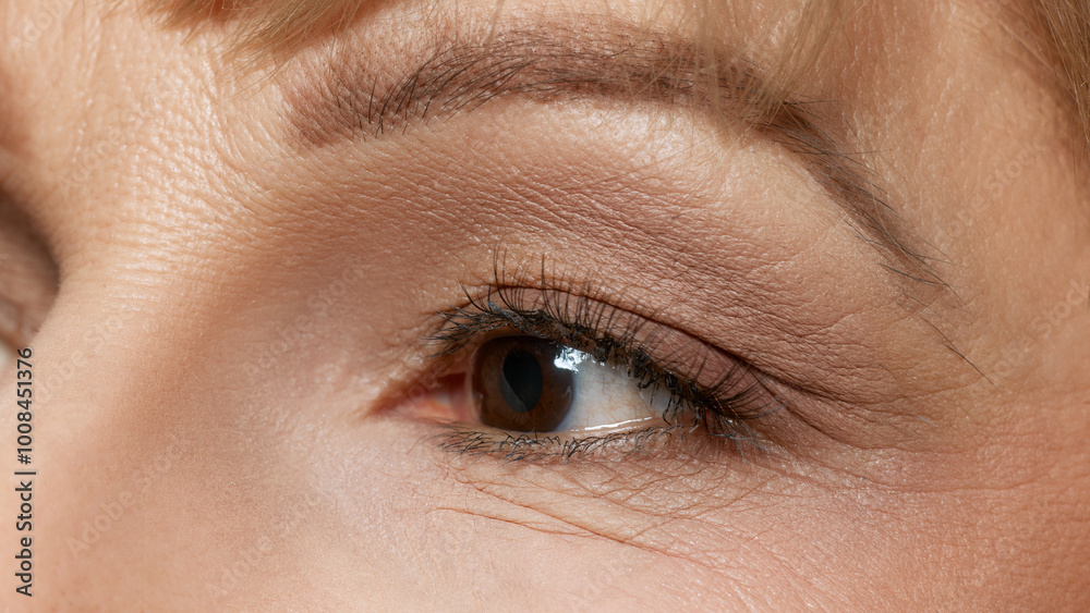 Obraz premium Extremely close up of middle aged beautiful woman with well-kept skin in preorbital, eye zone against white studio background. Concept of beauty, wellness, cosmetology, anti-aging products. Ad