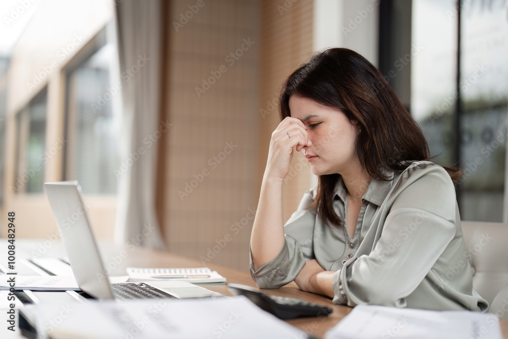 Obraz premium Stressed Business Woman Working at Desk with Laptop and Documents in Modern Office Environment