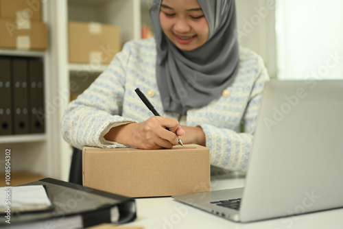Start up small business owner writing addressee details on cardboard box for delivery to customer