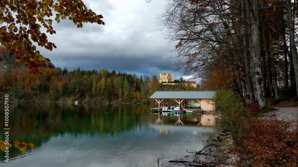 Panoramic view of the Alpsee lake in Autumn trees season and Bavaria Alps in background, beautiful reflections in water Panoramic view of the Alpsee lake in Autumn trees season and Bavaria Alps in background, beautiful reflections in water