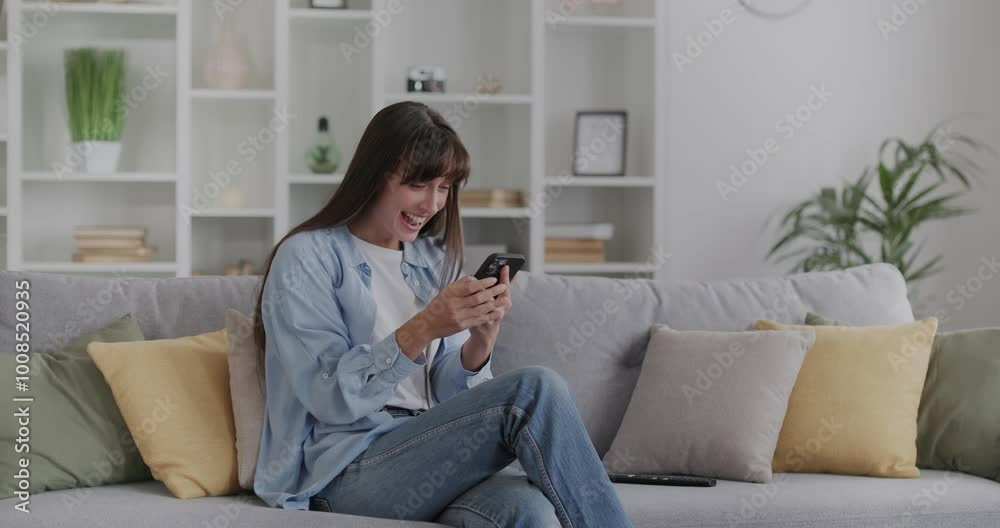 Young pretty woman sitting on a couch and uses smartphone, won a great prize. Young pretty woman sitting on a couch and uses smartphone, won a great prize.