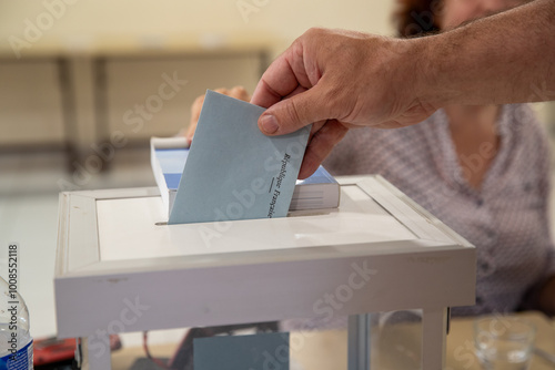 Vue d'une main d'un homme déposant son bulletin de vote dans l'urne lors d'une élection dans un bureau de vote en France.