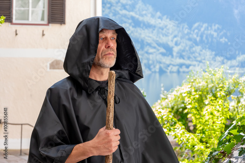 A monk in a black cassock and carrying a staff against a background of mountains and an old village house. photo