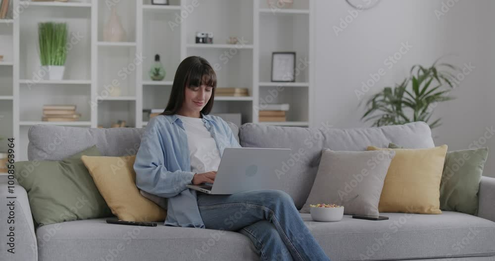 Beautiful woman sits on sofa, working at home on laptop, typing on keyboard. Beautiful woman sits on sofa, working at home on laptop, typing on keyboard.