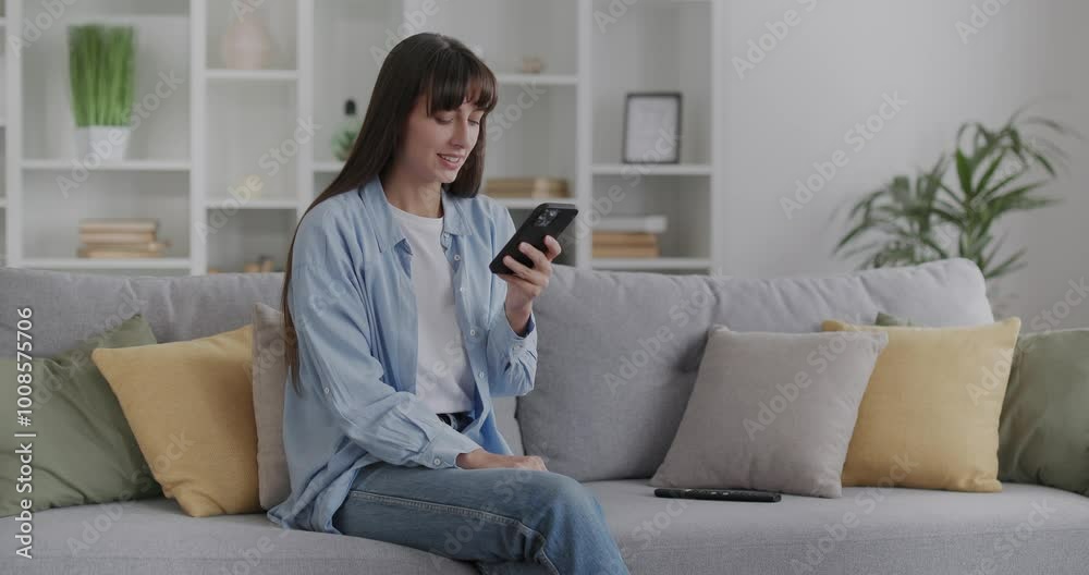 Young relaxed brunette woman sitting on a sofa, using her smartphone. Young relaxed brunette woman sitting on a sofa, using her smartphone.