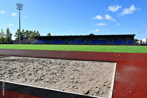 Fotografía an athletic stadium under clear blue skies, showcasing a long jump sandpit in th