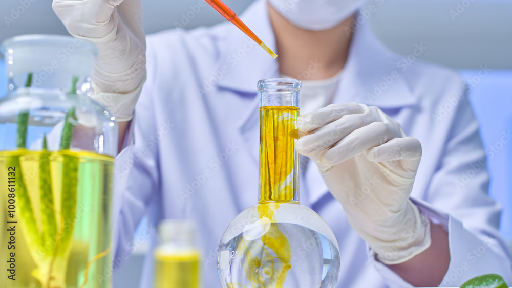 In a contemporary lab environment, a scientist is shown in a close-up picture taken from below, dumping yellow solution into a transparent flask and an aloe vera-soaked cork bottle. In a contemporary lab environment, a scientist is shown in a close-up picture taken from below, dumping yellow solution into a transparent flask and an aloe vera-soaked cork bottle.