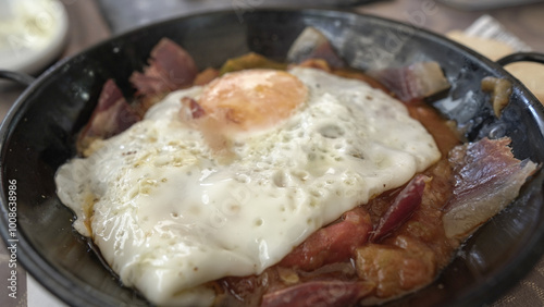 Primer plano de u huevo frito sobre revuelto de jamón , pisto de verduras y huevo frito servido en cazuela photo