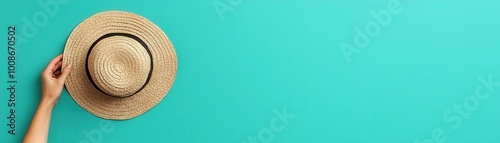 Hand holding straw hat against vibrant turquoise background, offering a summery vibe with plenty of copy space.