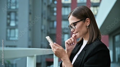 Young serious businesswoman using smartphone, office building background