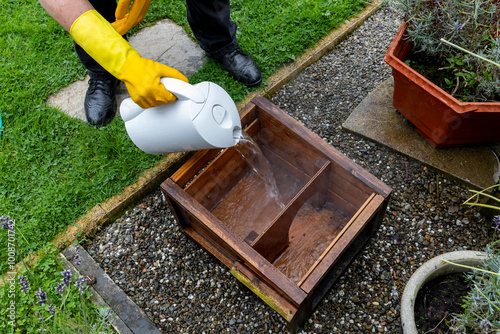 Woman wearing yellow rubber gloves cleaning and sterilizing wooden hedgehog house with boiling water photo