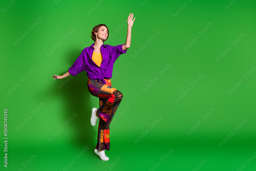 Photo of funny young woman in purple stylish shirt trendy baggy pants and brown bob haircut dancing isolated on green color background Photo of funny young woman in purple stylish shirt trendy baggy pants and brown bob haircut dancing isolated on green color background